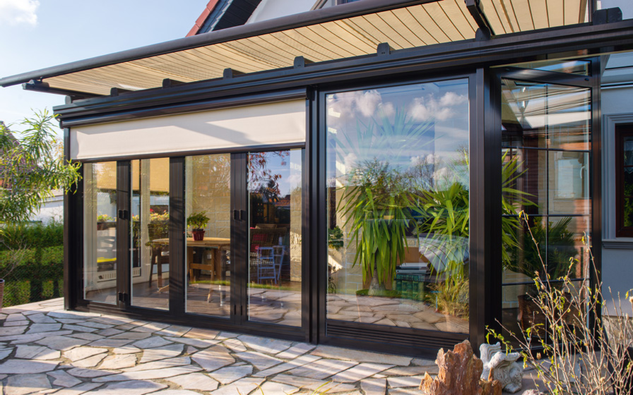 Senkrechte ZIP-Markisen an den Front- und Seitenelementen eines Wintergartens bieten effektiven Sonnenschutz bei gleichzeitig hoher Transparenz nach draußen.